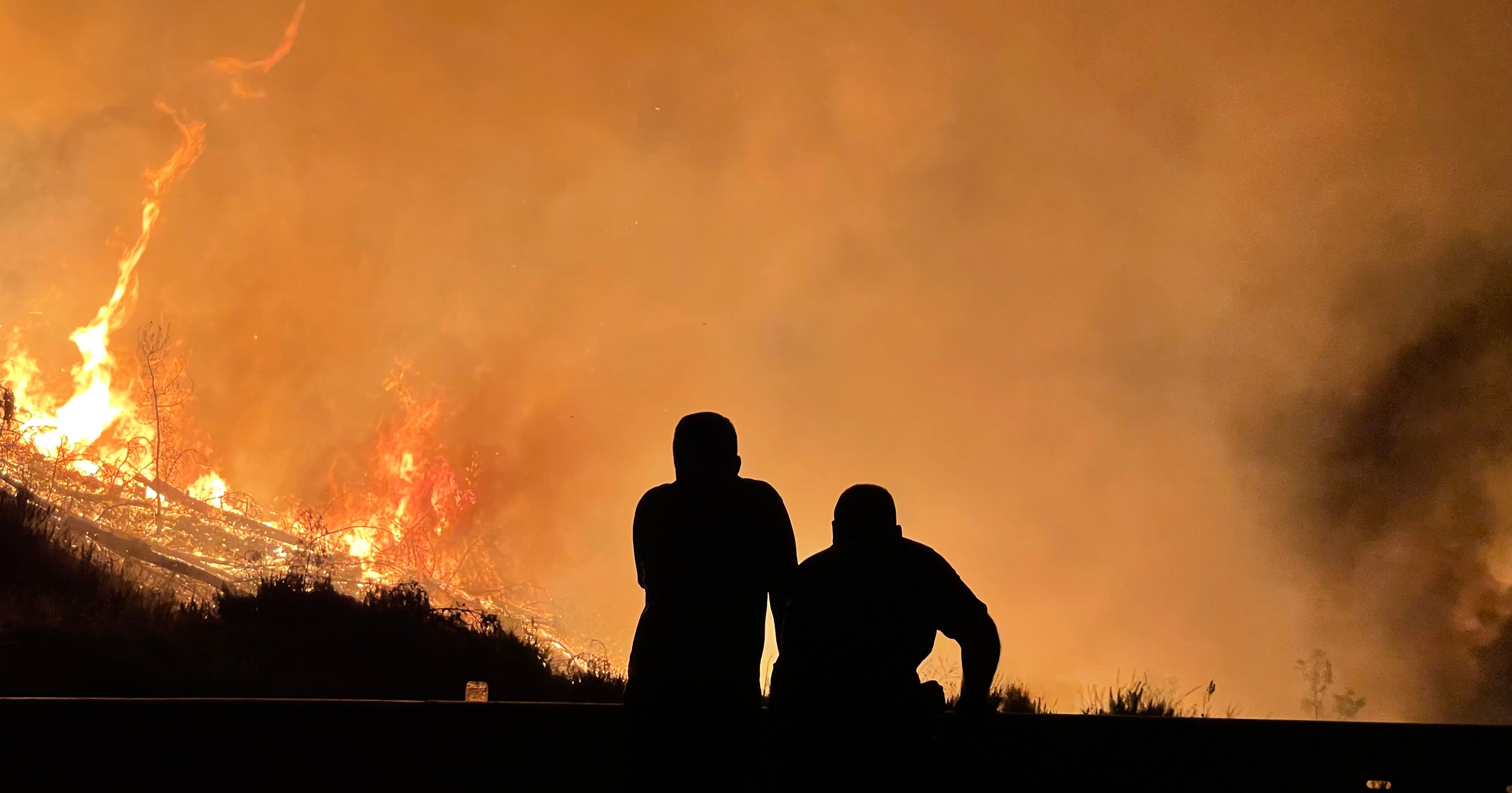 Deux personnes en silhouette devant un grand feu de forêt
